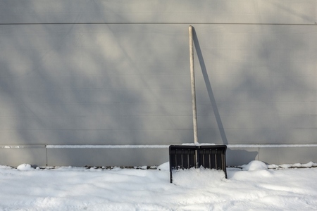 Snow shovel leaning against winter house wall
