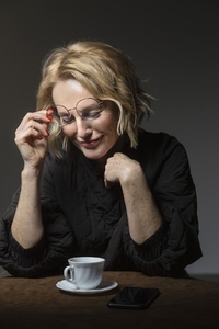 Smiling blonde woman lifting eyeglasses looking down at coffee