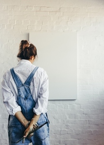 Pensive female painter standing in front of a blank canvas