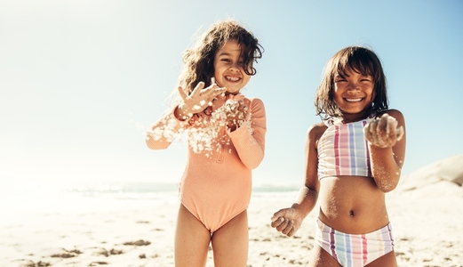 Cheerful little girls playing with sea sand at the beach