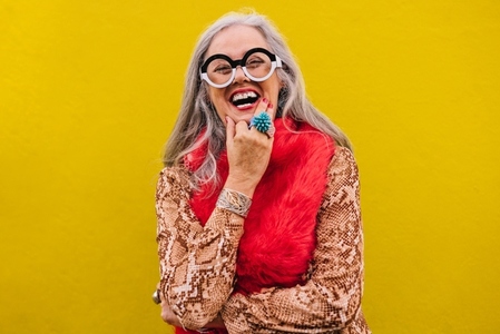 Happy senior woman laughing cheerfully against a lemon background