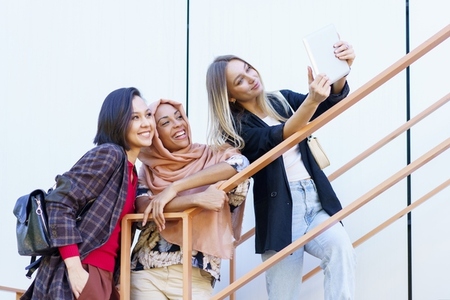 Excited young multiethnic female millennials smiling and taking selfie on tablet