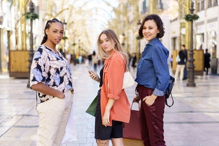 Multiracial female friends standing on city street with purchases