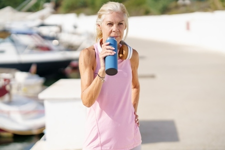 Mature sportswoman in fitness clothing drinking water from a metal fitness bottle outdoors