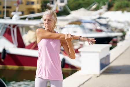 Fit elderly sportswoman stretching arms in port