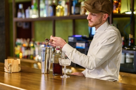 Male barkeeper pouring alcohol into shaker