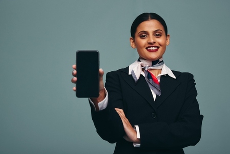 Modern flight attendant holding up a smartphone in a studio