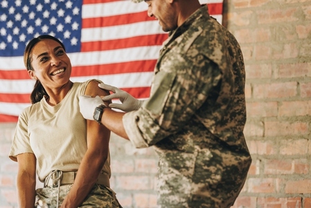 Carefree servicewoman smiling at the military nurse after vaccination