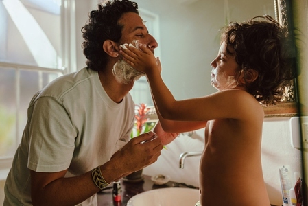 Young boy applying shaving cream on his father