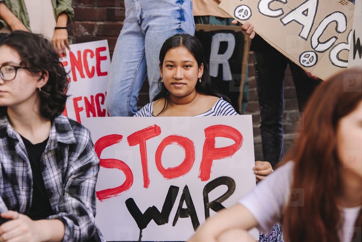 Confident young woman holding an anti-war poster during a protest