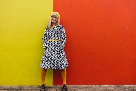 Cheerful senior woman looking away thoughtfully against a colourful wall