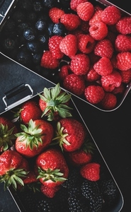 Flat lay of fresh berries in lunchboxes over dark background