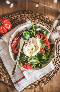 Italian salad with Buratta cheese in white bowl on table