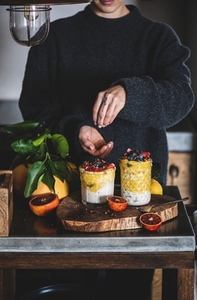 Woman putting ingredients to muesli with mango smoothie and granola