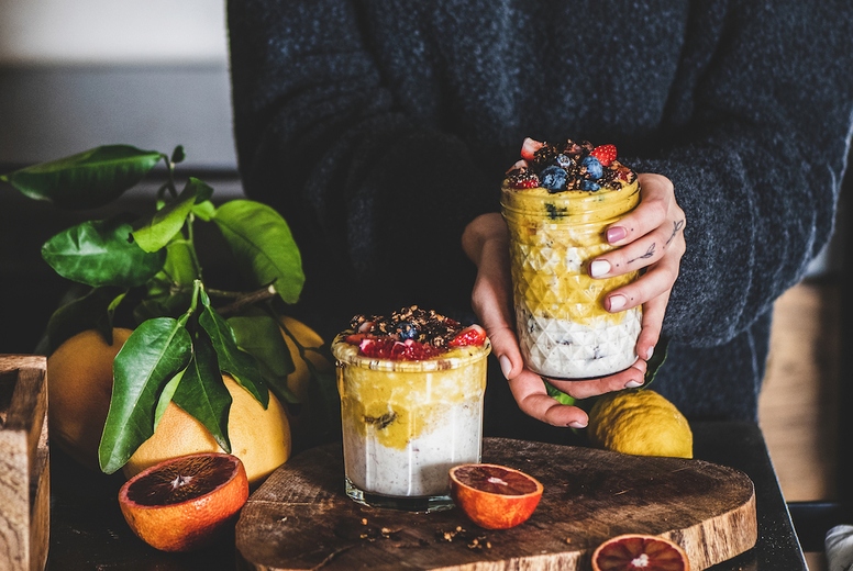 Woman holding glass of muesli with mango smoothie and granola