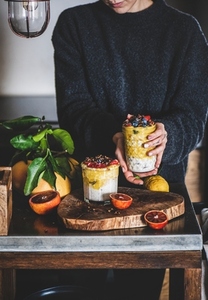 Woman holding glass of muesli with mango smoothie and granola