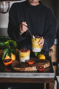 Woman eating muesli with mango smoothie and granola from glass