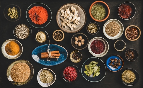 Flat lay of different spices in bowls over dark background