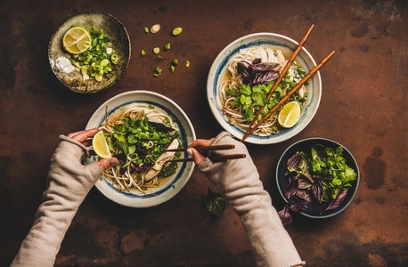 Womans hands with chopsticks and lime over vietnamese soup Pho Ga
