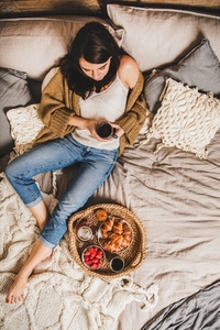 Young brunette woman sitting and having tasty breakfast in bed