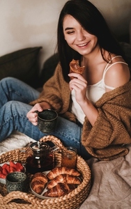 Young beautiful smiling brunette woman enjoying tasty breakfast in bed