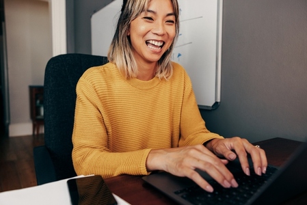 Cheerful businesswoman typing an email in her home office