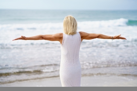 Anonymous mature woman with outstretched arms on seashore