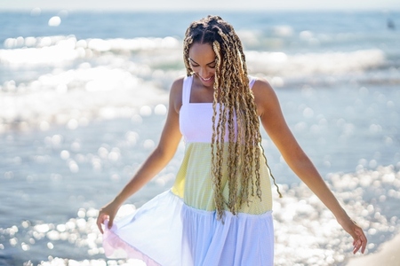 Black girl walking along the shore of the beach wearing a beautiful long dress