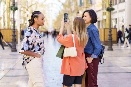 Diverse women taking selfie on smartphone in street