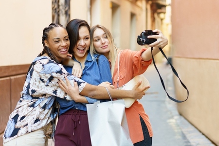 Carefree diverse women with photo camera spending time on street