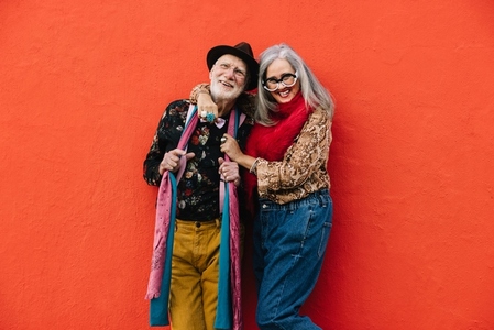 Carefree senior couple laughing together against a red wall