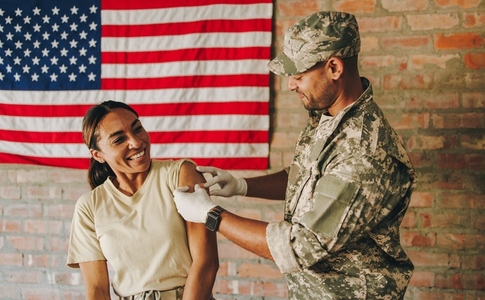 Young medic applying a band aid to a soldiers arm after vaccination