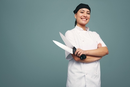 Smiling culinary chef holding two knives in a studio