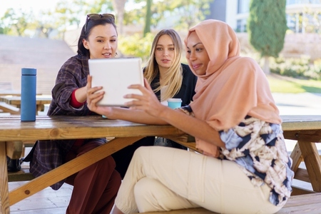 Cheerful diverse women sharing tablet during coffee break in cafe