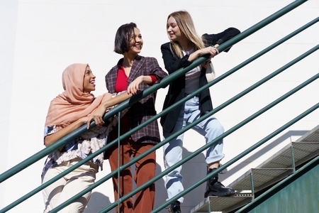 Content young diverse women looking away while standing on stairs in city
