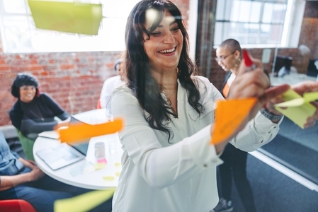 Smiling businesswoman sticking adhesive notes to a glass wall