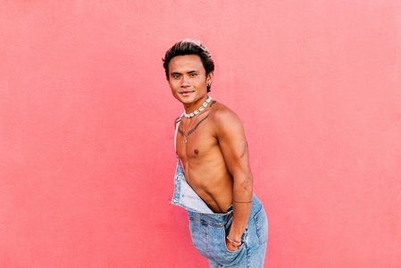 Young handsome guy posing outdoors against pink wall looking at camera