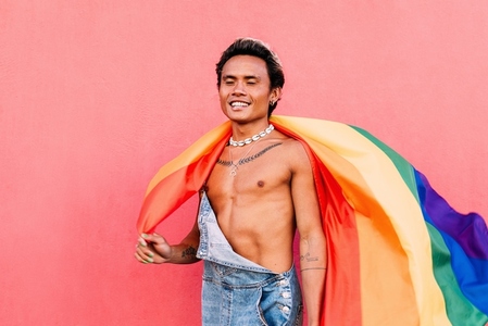 Happy male wearing overalls holding LGBT flag with closed eyes