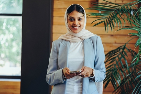 Happy Muslim businesswoman holding a smartphone in an office