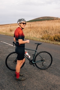 Full length of female cyclist with a bicycle standing on country road and looking away