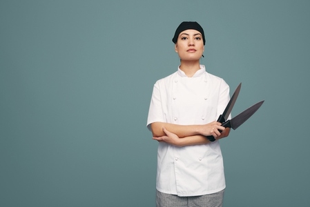Female culinary chef holding two kitchen knives in a studio