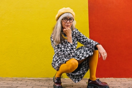 Pensive mature woman squatting against a colourful background