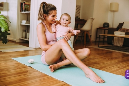 Cheerful mom smiling at her baby while sitting on an exercise ma