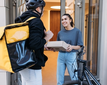 Smiling woman receiving a parcel from courier  Delivery guy with backpack giving package to a customer at an apartment building