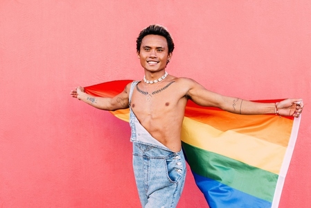 Young happy man walking outdoors with a rainbow LGBT flag looking away