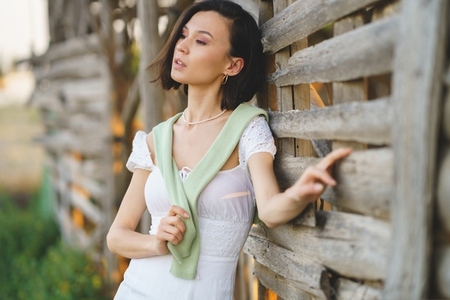 Asian woman  posing near a tobacco drying shed  wearing a white dress and green wellies