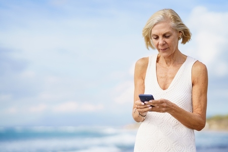 Mature woman walking on the beach using a smartphone