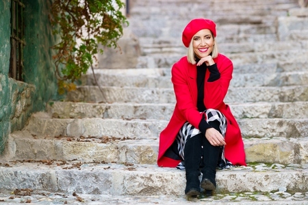 Feminine stylish woman resting on steps in town and smiling