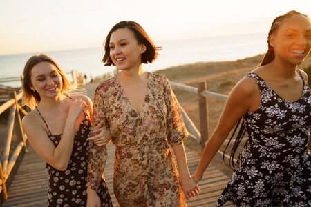 Content multiethnic girlfriends walking on footbridge on seashore