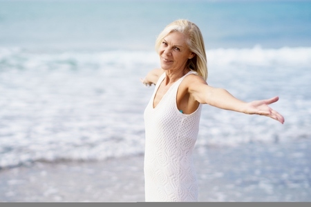 Mature female opening her arms on the beach  spending her leisure time  enjoying her free time